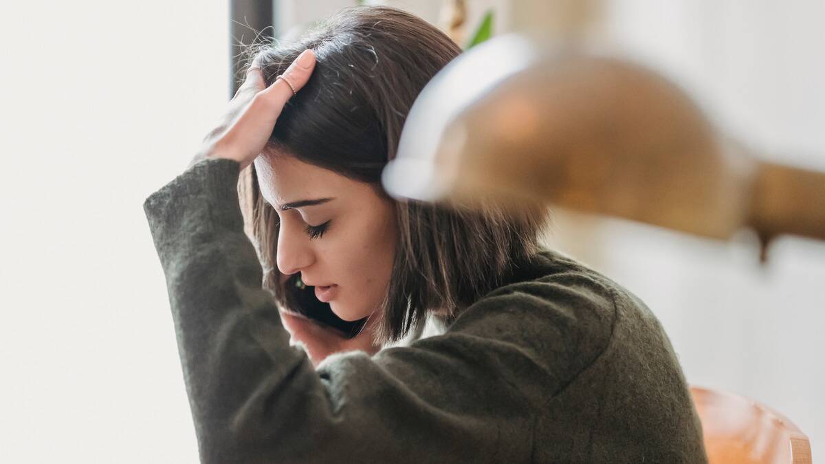 A woman on the phone sitting in her home with a hand on her head, looking frustrated.