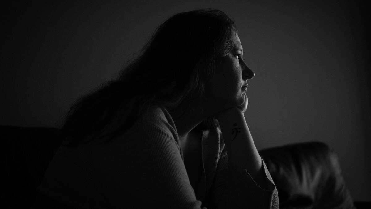 A greyscale image of a woman looking off to the side with her chin in her hand, seeming sad.