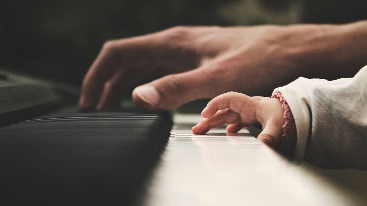 A close shot of a man's hand on a set of piano keys and his young child's smaller hand next to his.