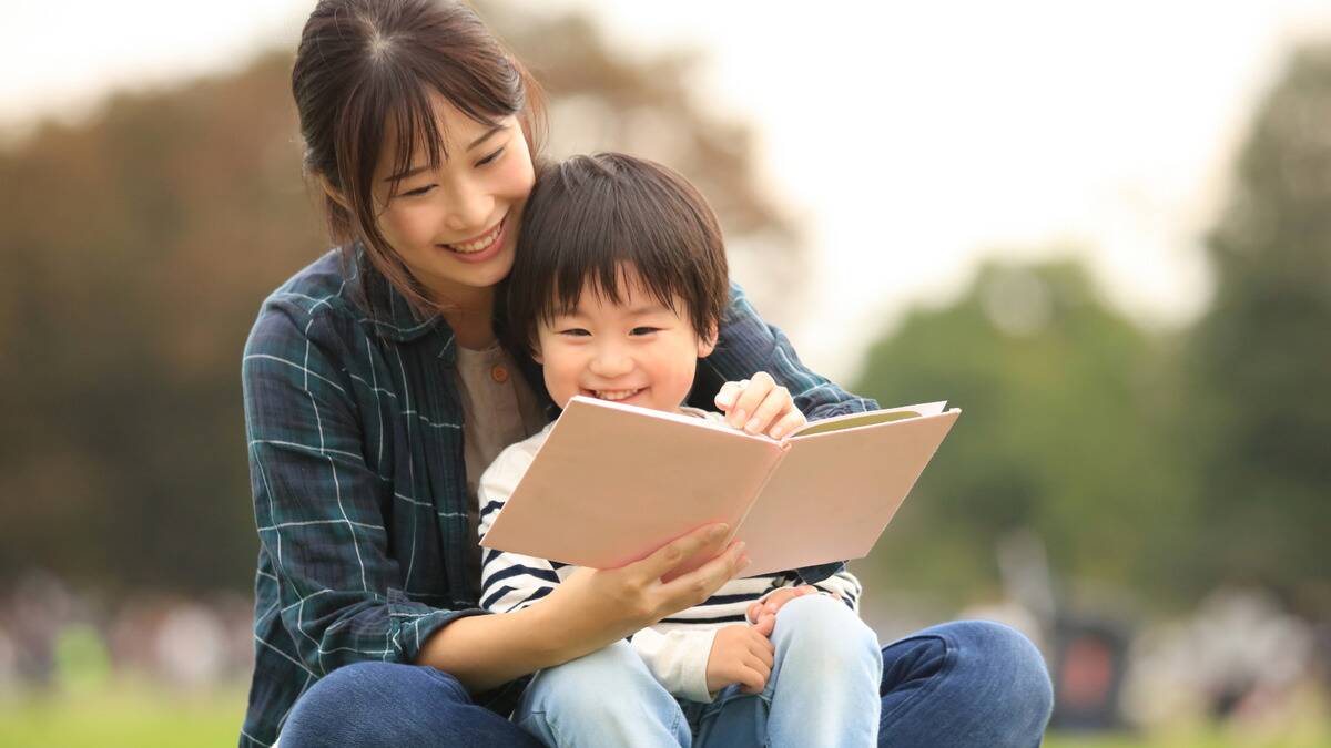 A woman holding her child in her lap, holding a book for him.