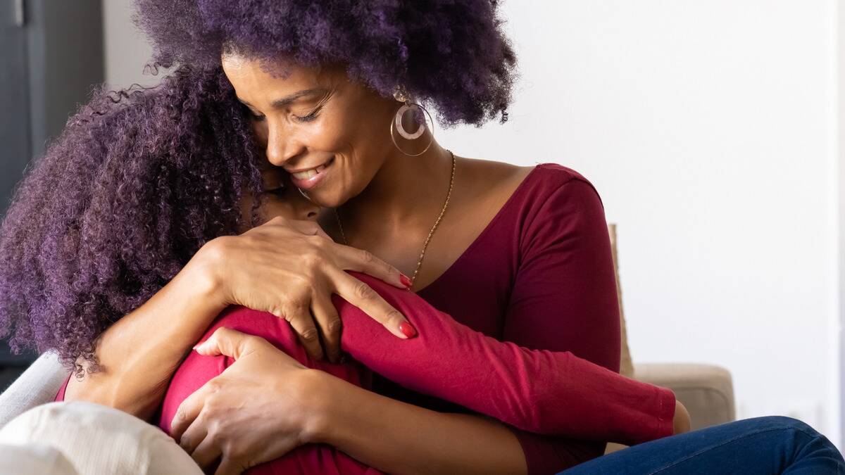 A close photo of a mother smiling as she holds her daughter in her arms.