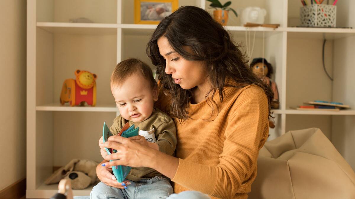 A woman holding her baby in her lap, holding a book for him.