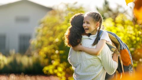 A woman carrying her daughter who's smiling brightly and wearing a large backpack.