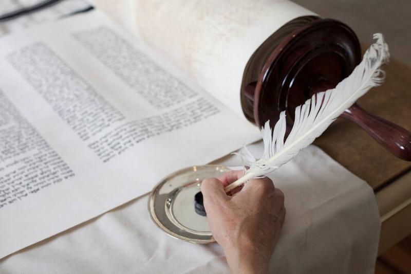 A scribe dipping a feather pen in ink in front of a large scroll.