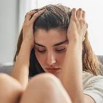 A close photo of a woman sitting on the ground, knees drawn up, hands in her hair.