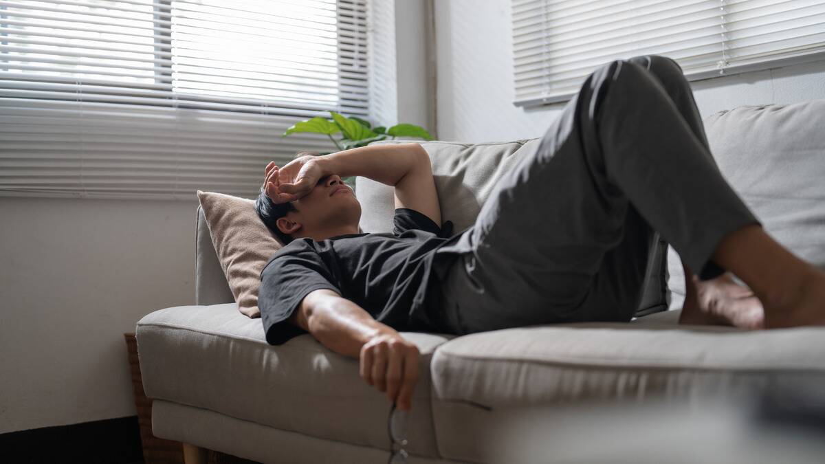 A man laying on his back on a couch, his arm over his eyes.