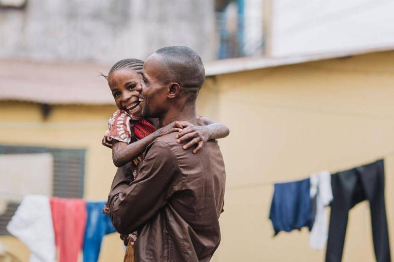 Gamai hugging her father with a bright smile as he carries her.