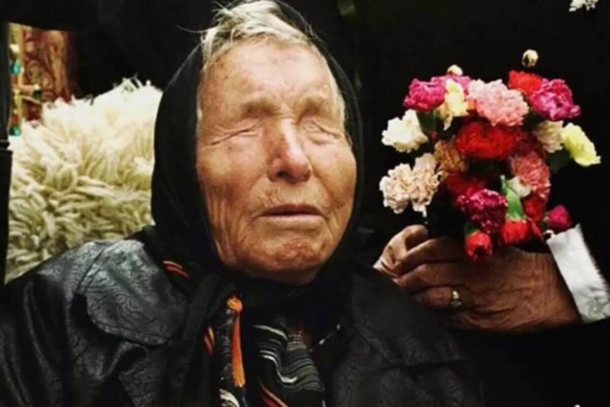 A closer photo of Baba Vanga sitting up, some people behind her, one holding a bouquet of flowers.