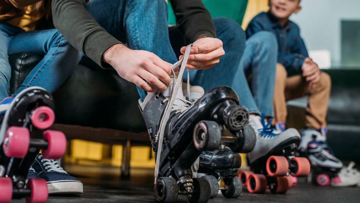 A photo of someone lacing up their roller skates, sitting next to other people already in skates.