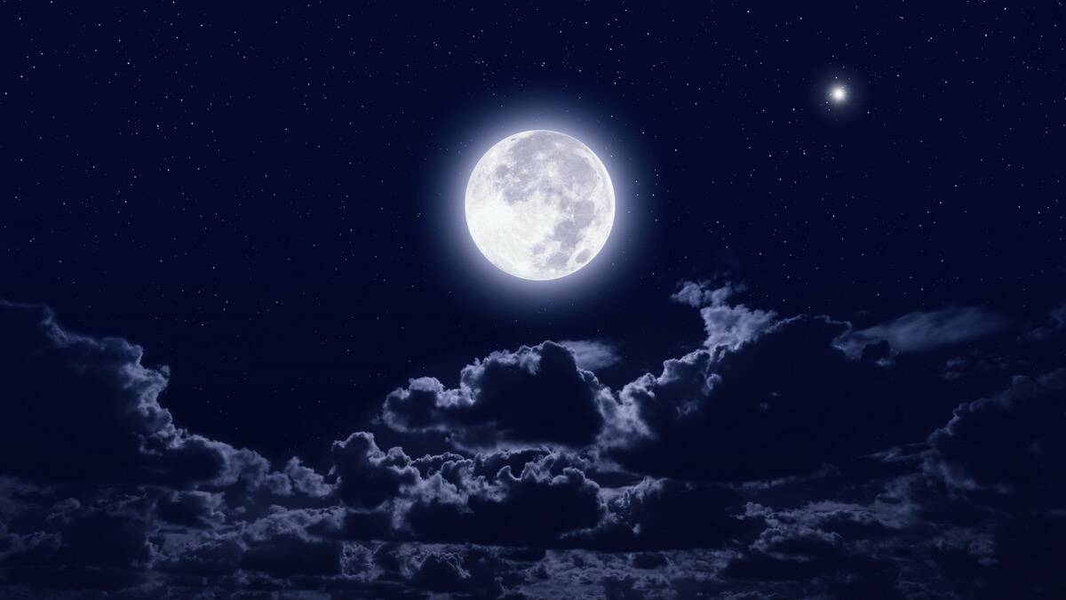 A bright, glowing full moon in a dark blue night sky, above some clouds.