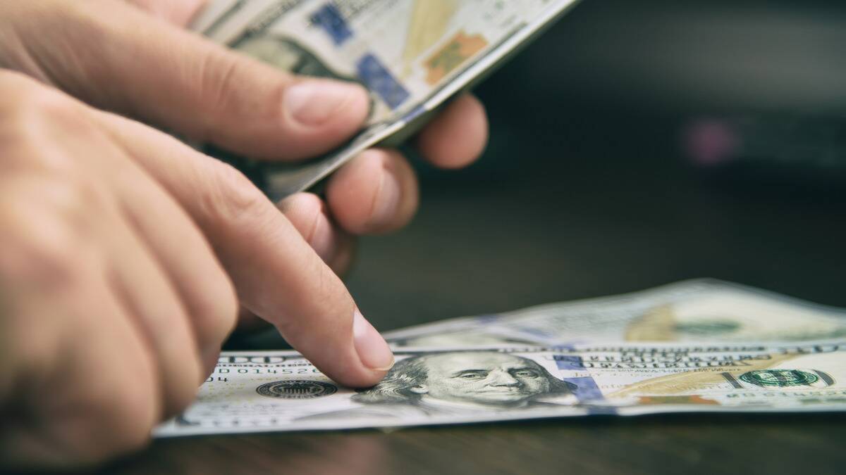 A very close photo of someone counting a stack of bills, their finger atop a bill they just placed on the table.