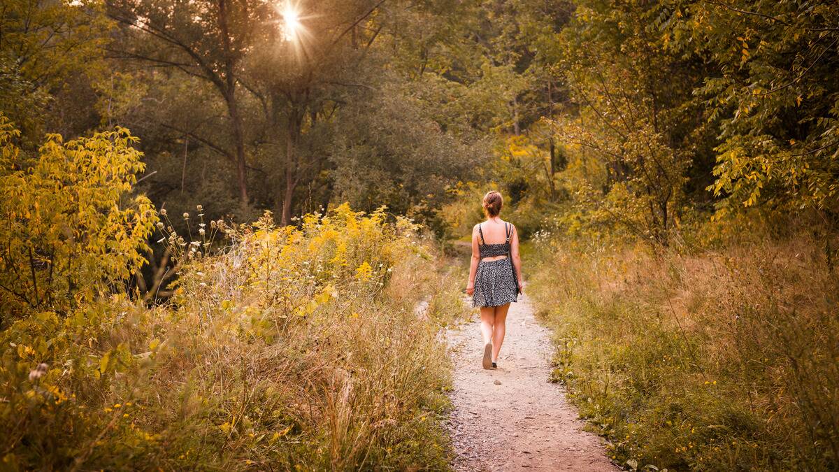 A woman walking down a dirt path in a grassy forest.