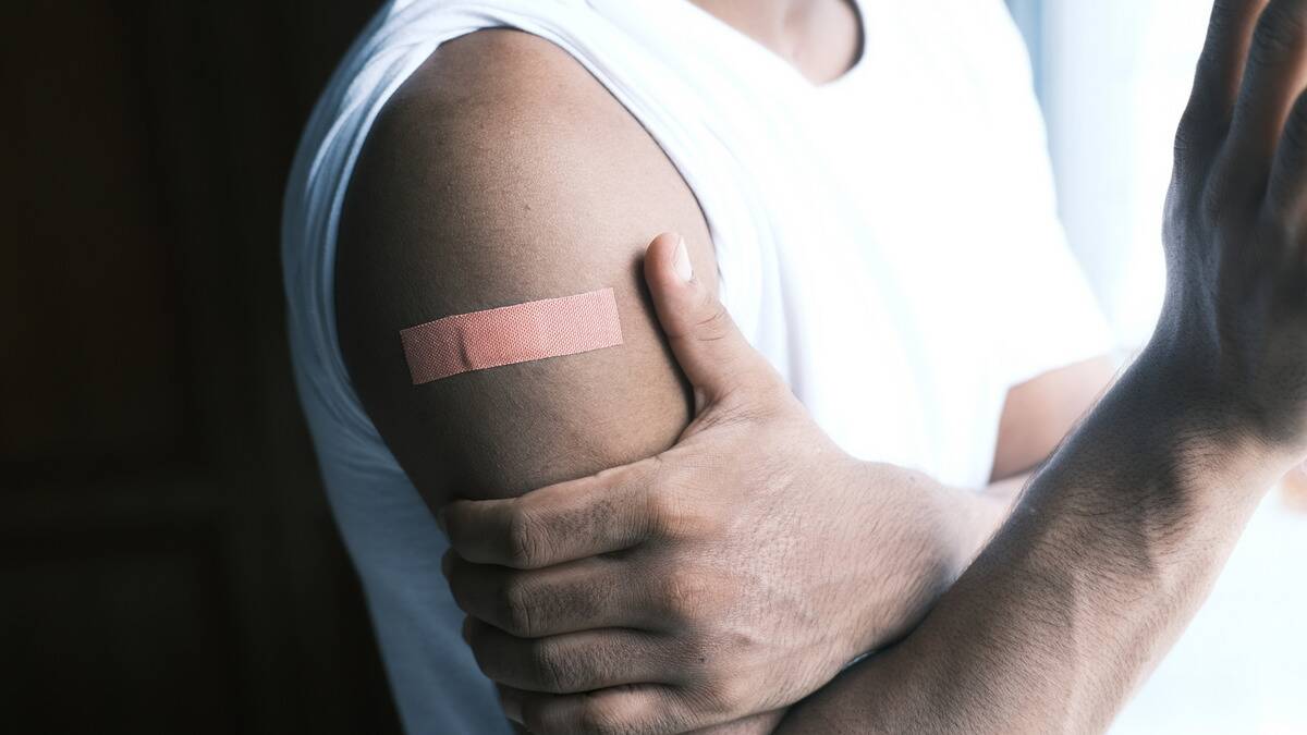 A man grabbing his arm that has a bandaid stuck on it.