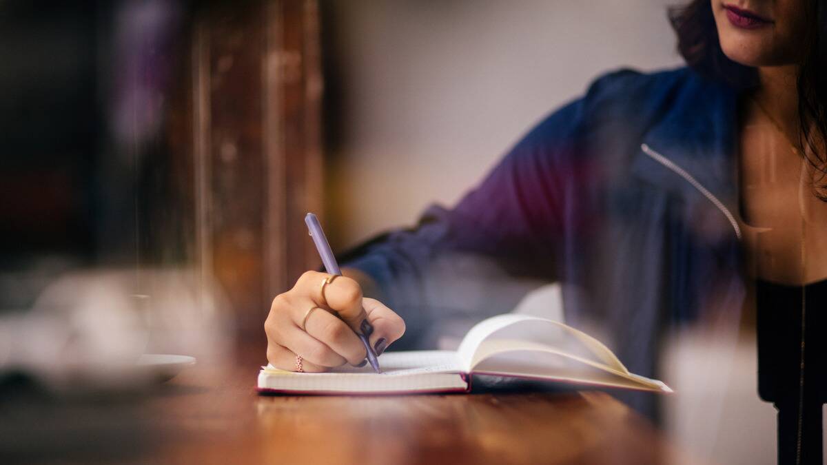 A woman writing in a journal on a table.