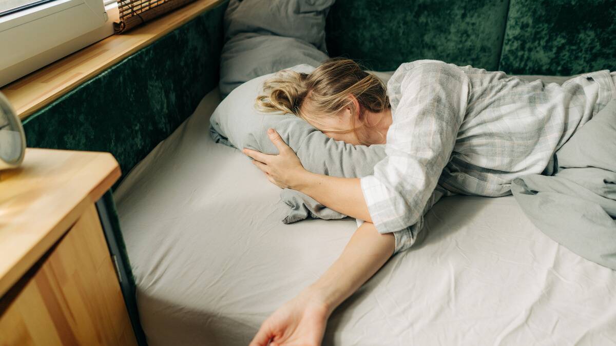 A woman in bed, her face burried in her pillow, sleeping on her side.