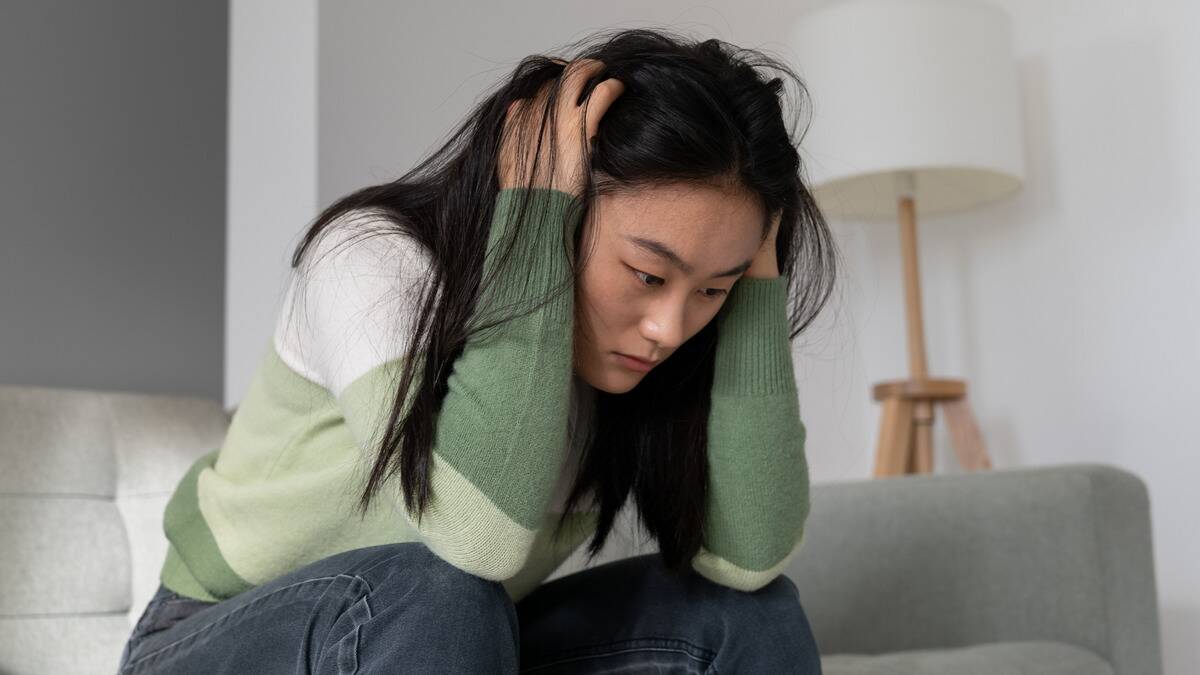 A woman sitting on her couch, hands on the sides of her head in her hair.