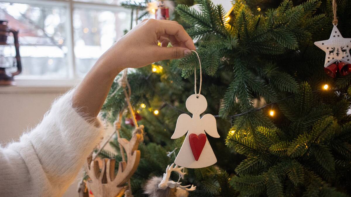 A close photo of someone hanging an angel ornament on a branch of their Christmas tree.