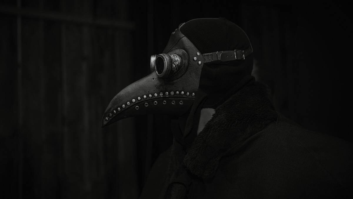 A dark greyscale photo of someone wearing a plague doctor mask.