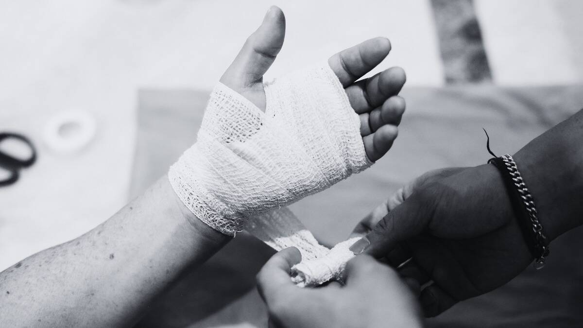 A black and white photo of someone wrapping another person's hand in bandages.