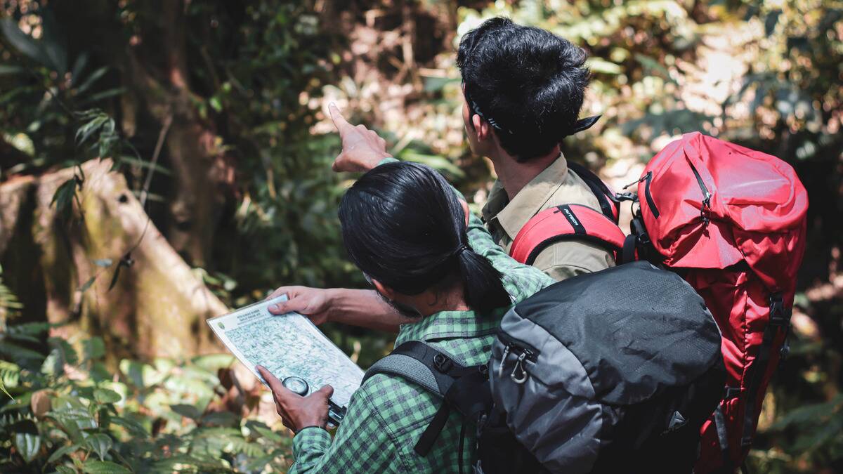 Two people hiking a trail, one pointing to the distance as the other looks at a small paper map.