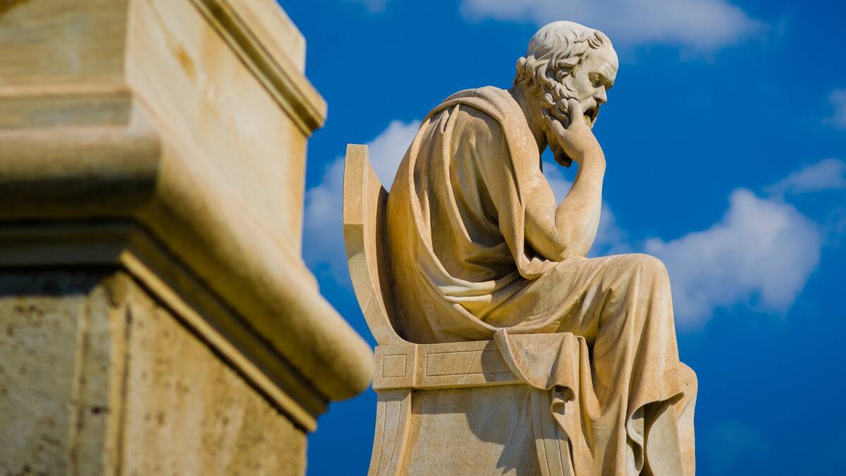 A stone statue of a philosopher under a bright blue sky.