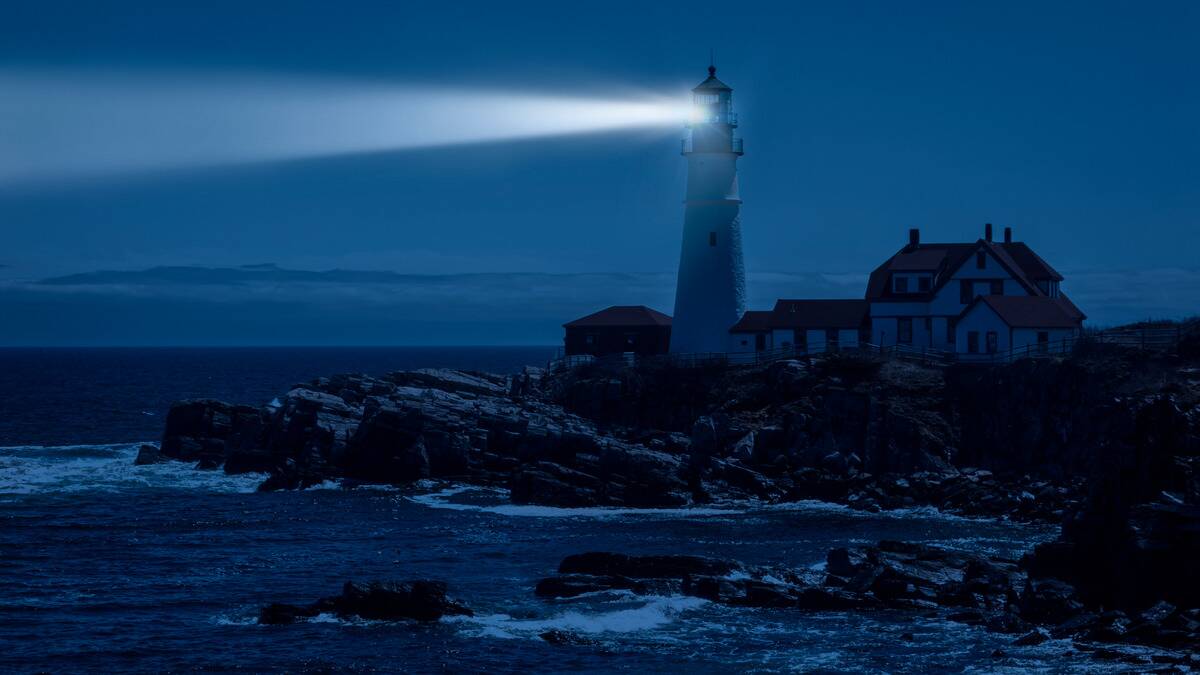 A blue-toned photo of a lighthouse on a rocky outcrop.