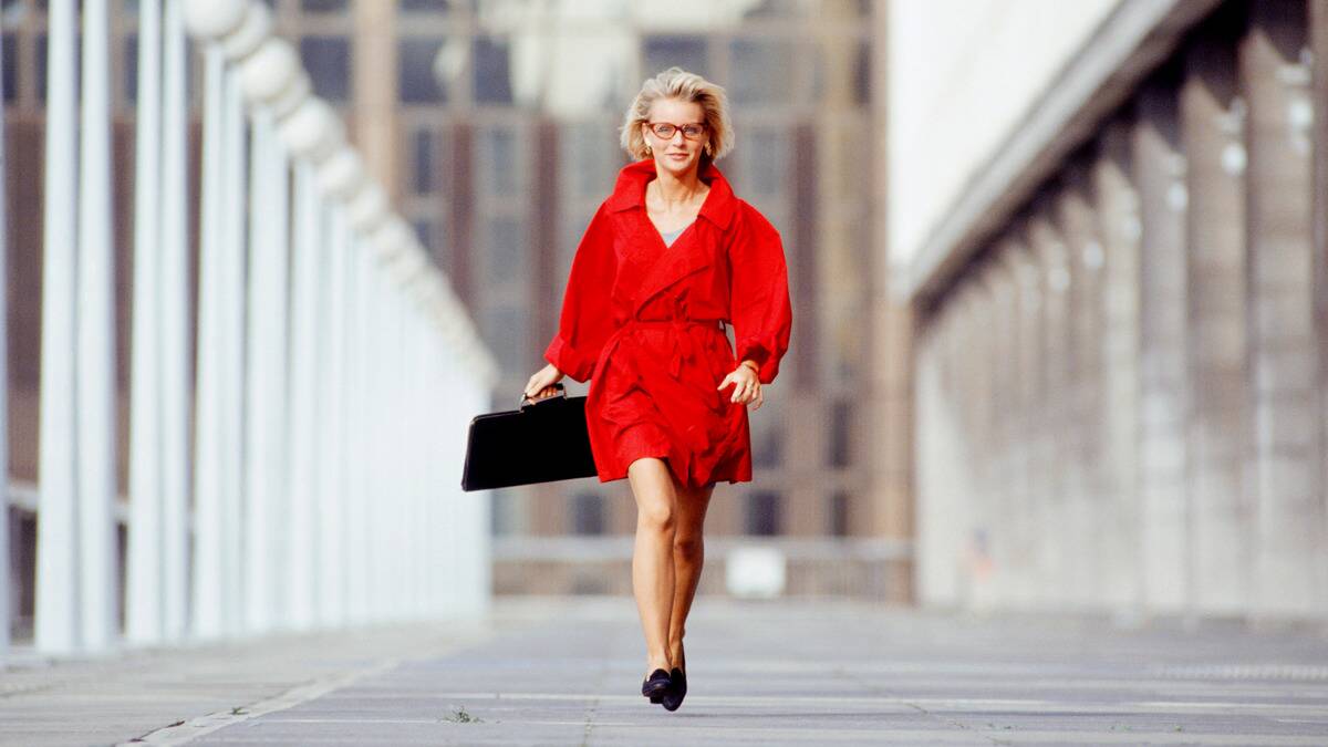 A woman in a bright red coat walking confidently down the street toward the camera.