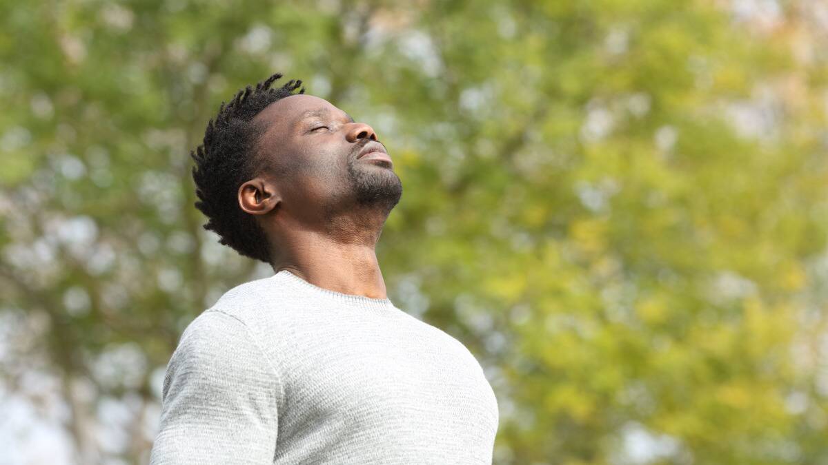 A man standing outside with his head tilted up, eyes closed, seeming to be inhaling.