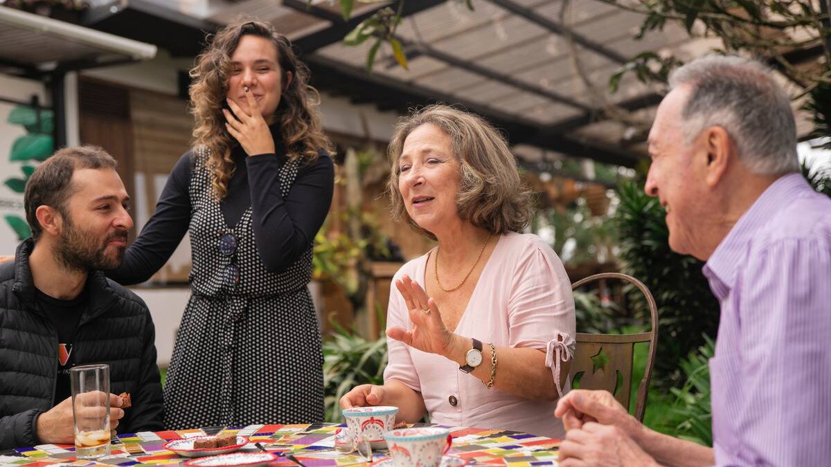 A gamily gathered around an outdoor table, one woman speaking and the rest listening.