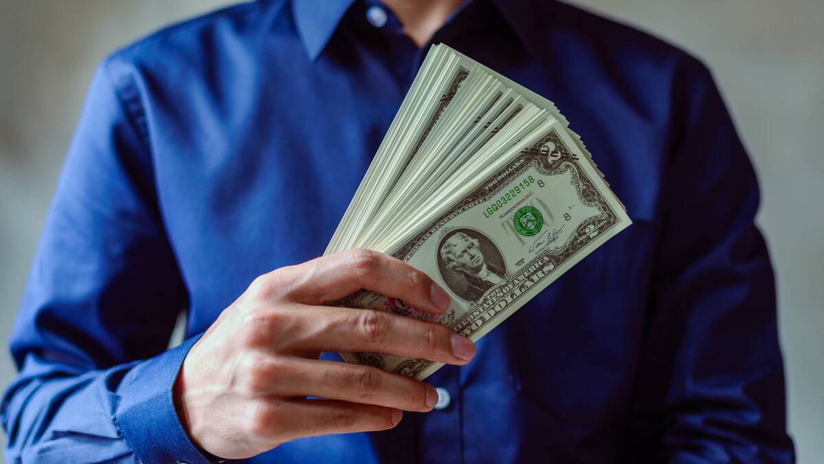 Someone in a bright blue buttonup shirt, holding a slightly fanned out stack of $2 bills.