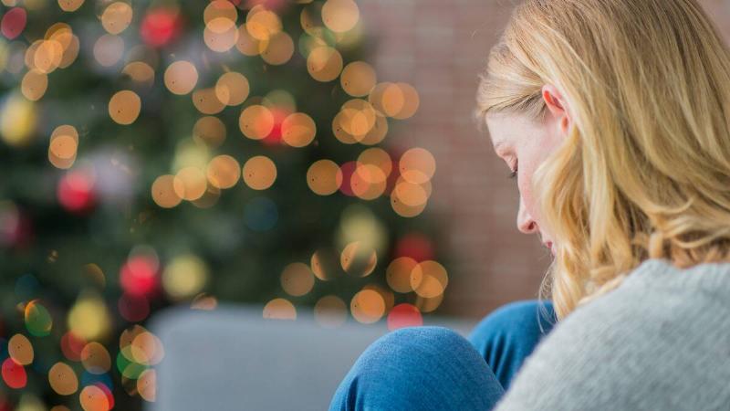 A close behind-angle shot of a woman on a couch, her Christmas tree shining behind her.