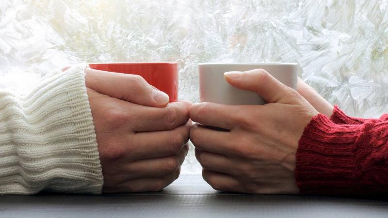 A close photo of a pair of hands positioned across from one another, each cupping a mug in their hands.