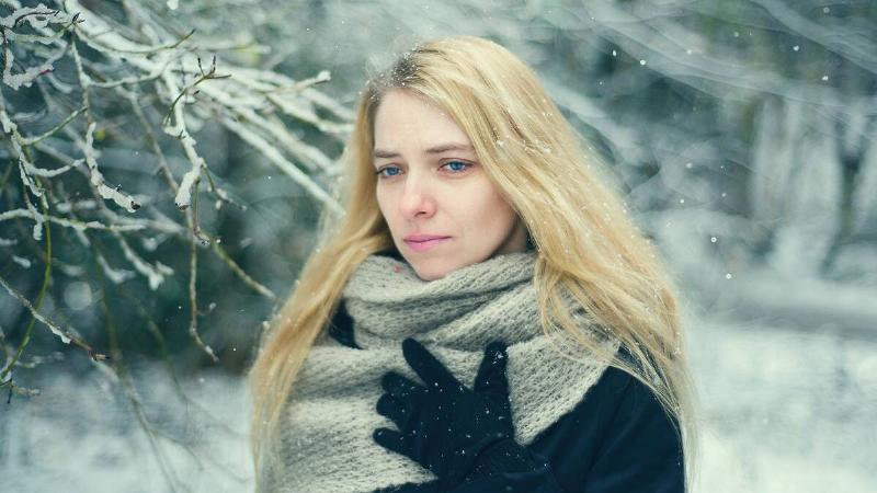 A woman walking outside in the snow, looking sad.