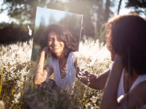 woman smiling in the mirror ro herself in a field