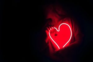 person in dark lighting holding red LED heart