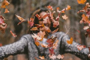 woman throws fall leaves into the air in front of her