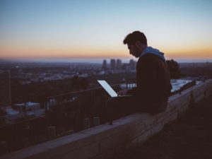 man working on his laptop on a roof by sunrise