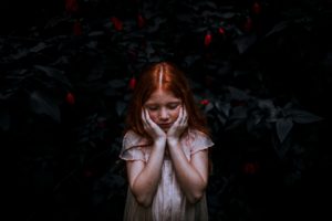 redhead little girl stands with her eyes closed and her hands on her cheeks