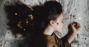 young girl lays in bed with her hair covered in gold stars and eyes closed