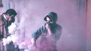 man in hoodie covers his face from pink fumes