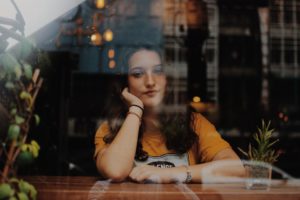 woman looking out coffee shop window with hand on her cheek