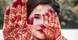 woman puts one hand forward and the other on her eye as hey're covered in henna