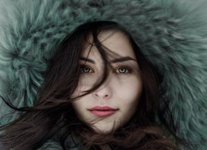 Woman with fur coat hood on her head and hair blowing in front of her face