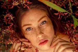 woman with freckles lays down by flowers