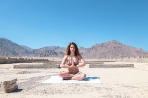 woman meditating in two piece bathing suit in a desert with hills