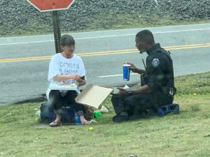 police officer and homeless woman eat pizza lunch on grass