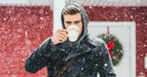 man drinking out of mug while snow falls around him