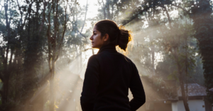 woman stands in the sunlight coming through the trees